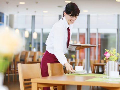 Mitarbeiterin des Hotels Franz deckt im Frühstücksbereich die Tische ein.